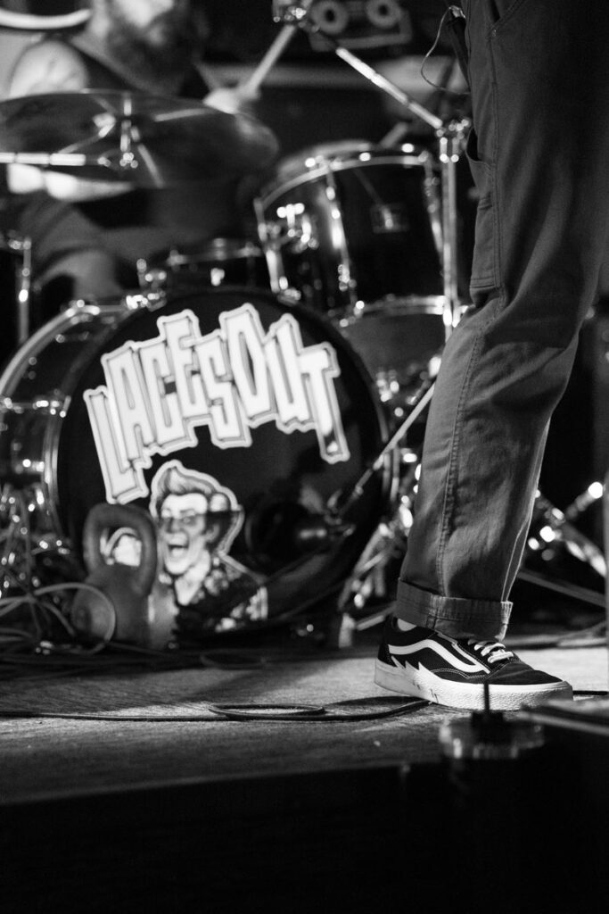 Black and white detail of the Laces Out bass drum head and a boot at the stage edge