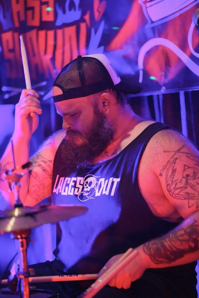 Laces Out drummer raising a stick mid-song behind the kit in a Laces Out tank top