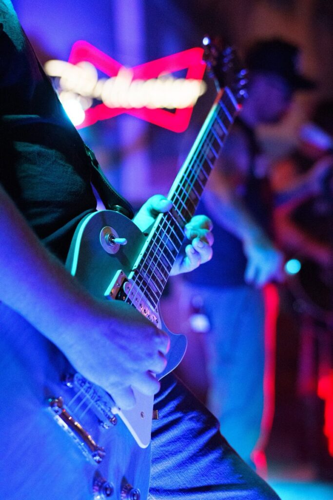 Close-up of a guitar being played, neon bar sign glowing behind